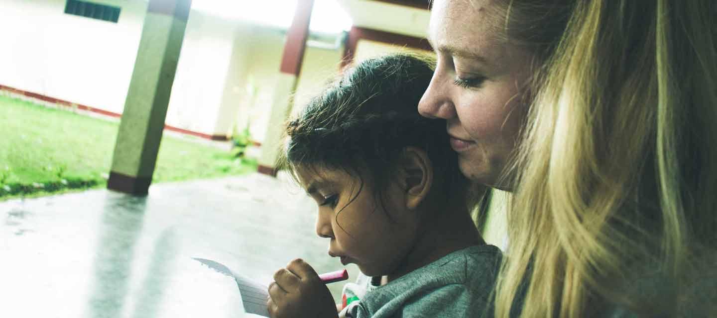 A student looks over a young girl's shoulder as she writes on a piece of paper