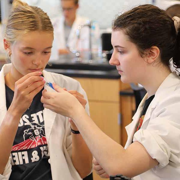 Two BCYC Immersion chemistry track students in lab coats analyzing test tube